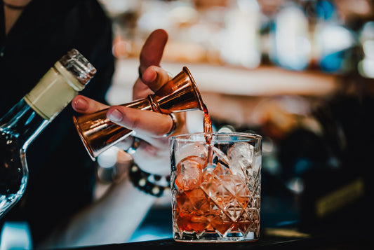 Bartender pouring red vermouth into an old fashioned glass with ice