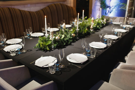 Glasses, forks, knives, napkins, candles and decorative flower on dark black tablecloth on table served for dinner
