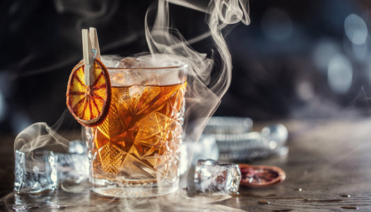 Smoked old fashioned cocktail with cubes of ice around on a dark background